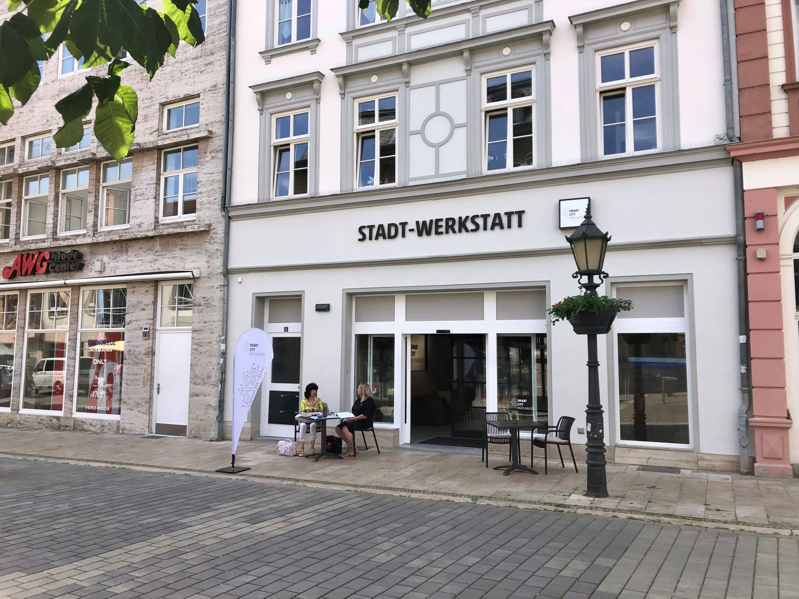 Gebäude der Stadt-Werkstatt mit Tischen und Stühlen im Außenbereich und einer Stehlampe.