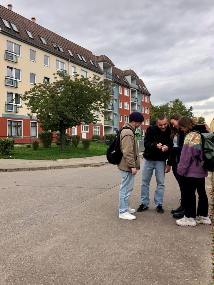 Vier junge Menschen stehen auf einer Straße und schauen auf ein Mobilgerät.