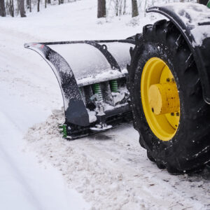 Schneepflug an einem Traktor Schneepflug montiert an einem Traktor auf einem verschneiten Weg im Wald.