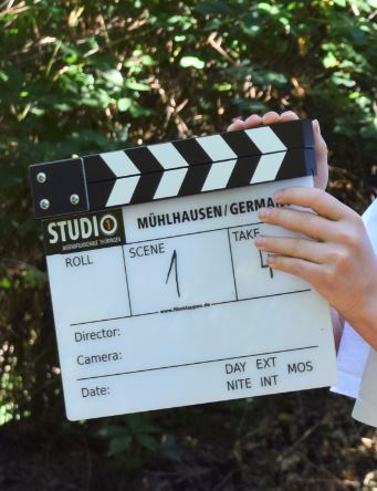 Filmklappe mit der Aufschrift 'Mühlhausen/Germany', Szene 1 und Take 1 in einem Wald.