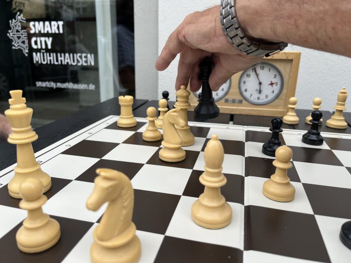Ein Spieler bewegt eine weiße Schachfigur auf einem Schachbrett mit schwarzen und weißen Figuren.