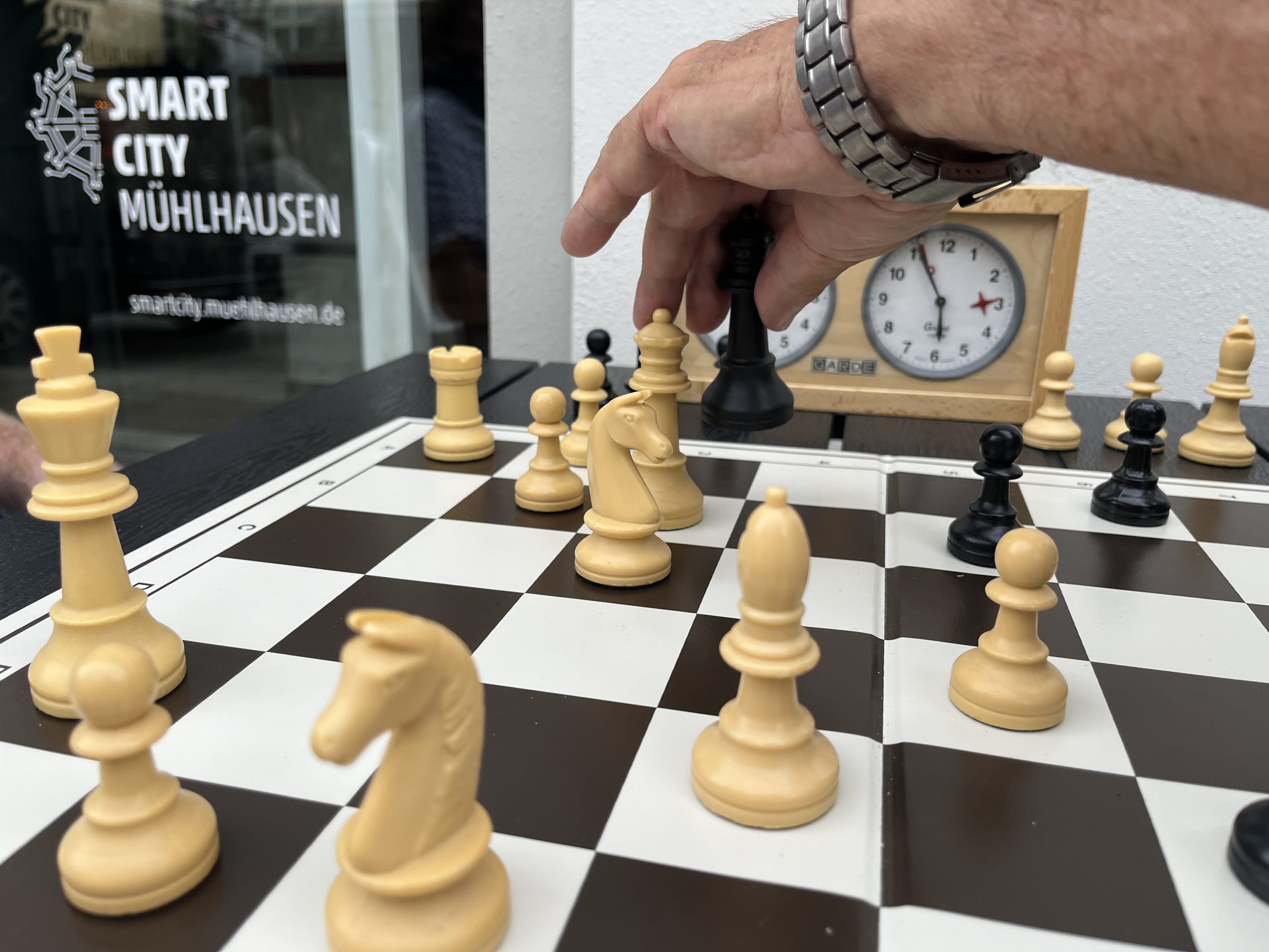 Ein Spieler bewegt eine weiße Schachfigur auf einem Schachbrett mit schwarzen und weißen Figuren.