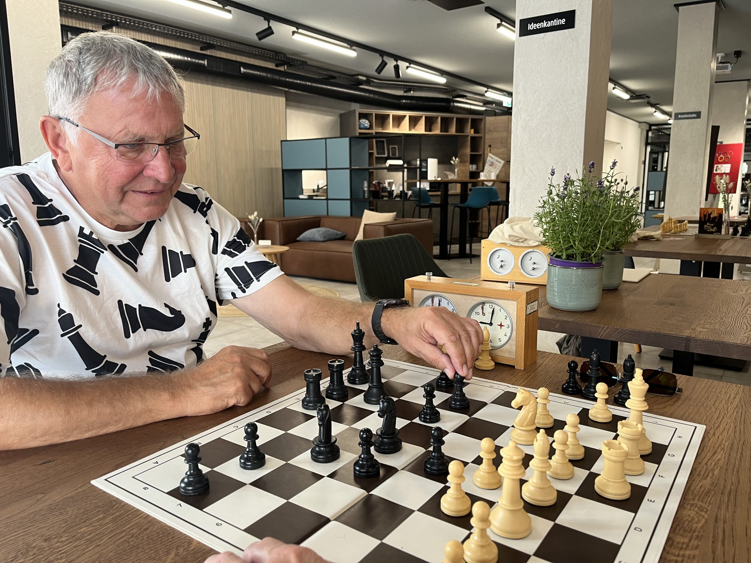 Ein Mann spielt Schach mit Holzfiguren auf einem Schachbrett in einem modernen Raum.