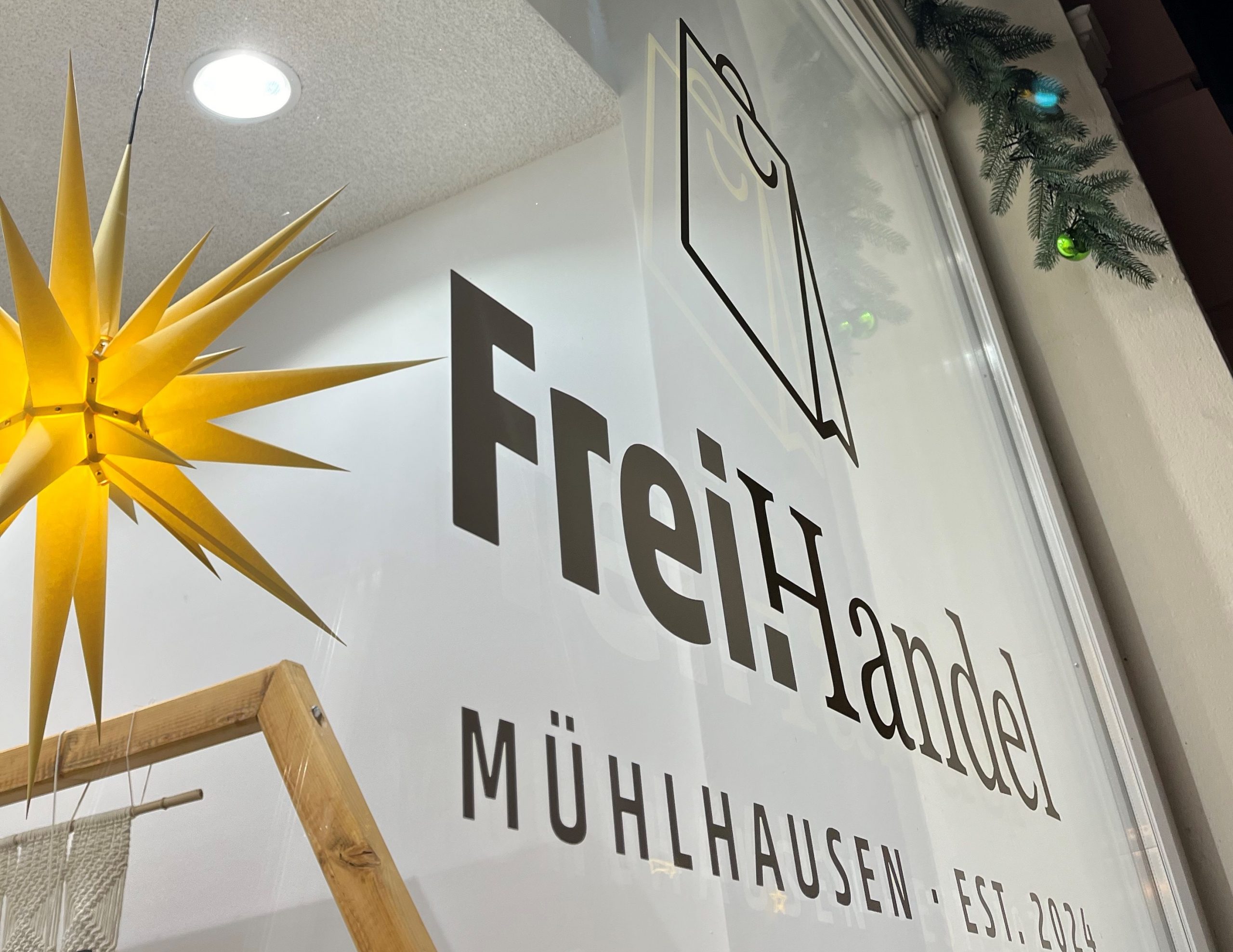Logo von FreiHandel mit einer gelben Dekoration in einem Schaufenster in Mühlhausen.