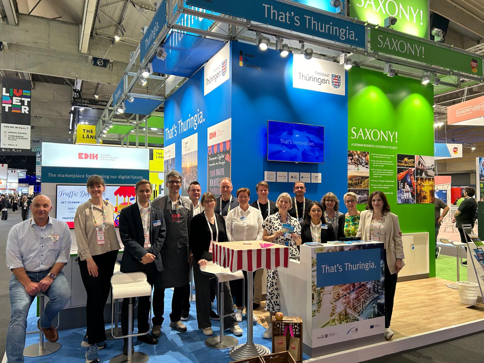 Messestand von Thüringen mit mehreren Personen, die an einem Tisch stehen und lächeln.