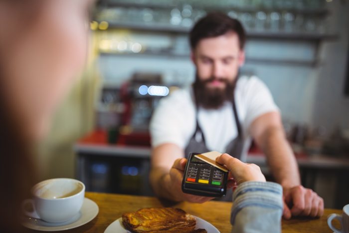 Eine Person reicht eine Kreditkarte an einen Barista in einem Café zur Zahlung für eine Speise.