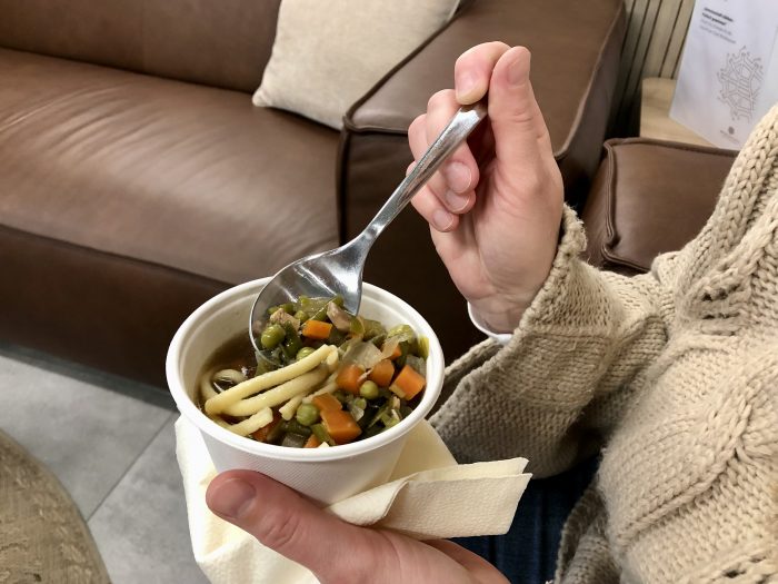 Eine Person hält eine Schüssel mit Gemüsesuppe und einem Löffel in der Hand.