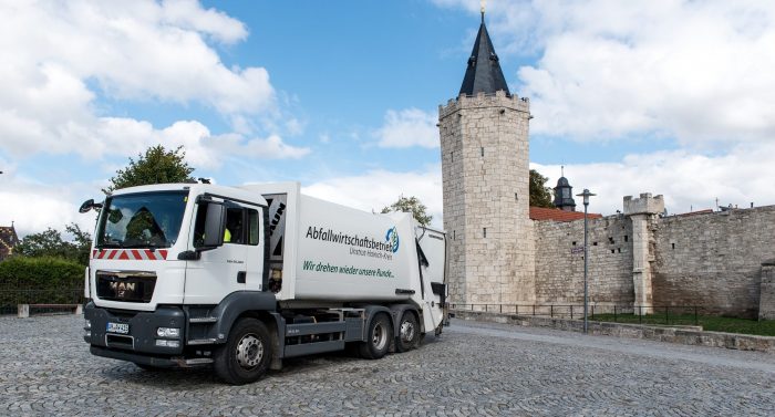 Ein Abfallwirtschaftsfahrzeug steht vor einer historischen Mauer mit einem Turm in der Nähe.