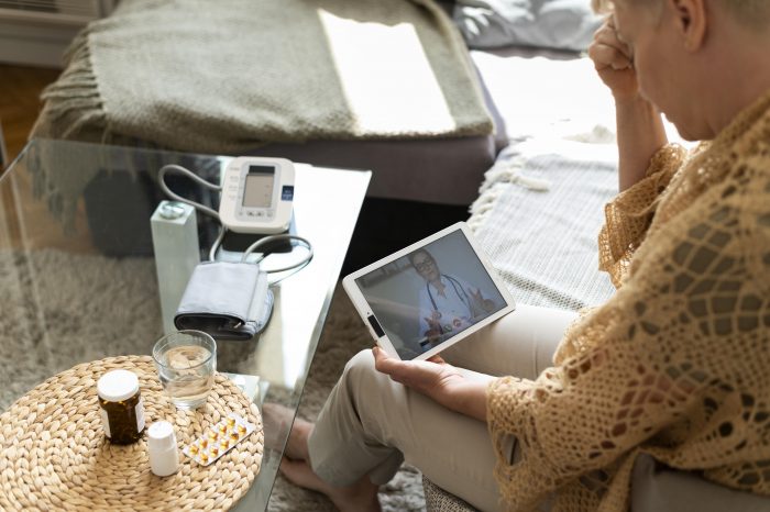 Eine Frau sitzt auf einem Sofa und spricht über ein Tablet mit einem Arzt während einer telemedizinischen Sitzung.