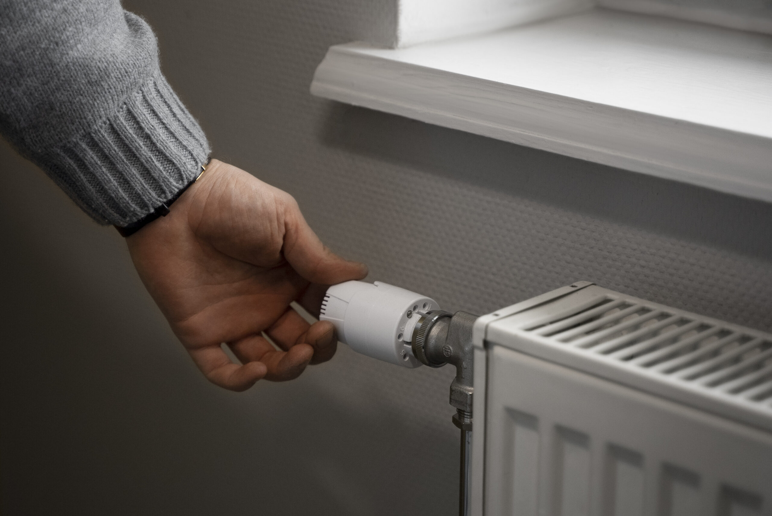 Eine Hand dreht das Thermostat eines Heizkörpers in einem Raum.