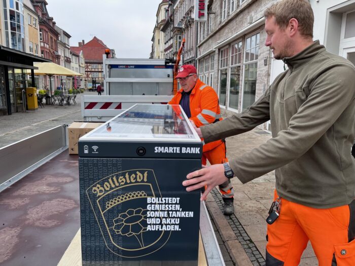 Zwei Männer vom Bauhof transportieren die Smarte Bank mit Solarpanelen nach Bollstedt.