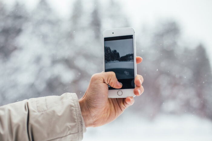 Eine Hand hält ein Smartphone, das eine Winterlandschaft mit Schnee zeigt.