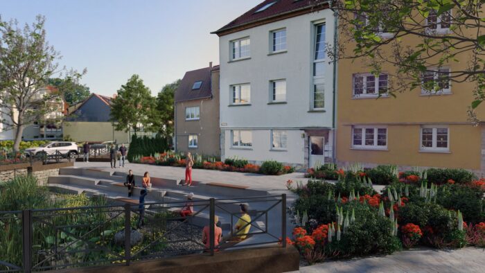 Im Innenhof vor einem weiß-gelben mehrstöckigen Gebäude laufen Jugendliche über den gepflasterten Schulhof, links verlaufen Wege, rechts säumen Blumenbeete das Gelände.