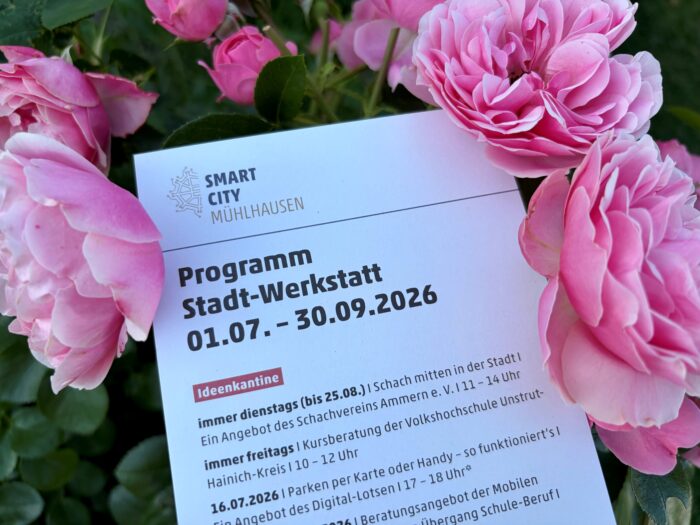 Rosa Rosen umrahmen ein Blatt mit dem Programm der Stadt-Werkstatt von Smart City Mühlhausen für Juli bis September 2026 und mehrere Termine.