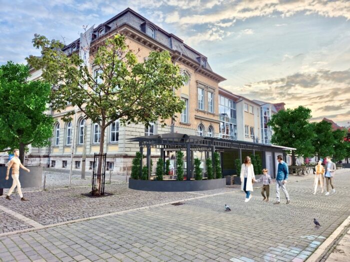 Vor einem historischen Gebäude mit Café-Pavillon spazieren Familien und Paare über einen gepflasterten Platz unter einem hellen Abendhimmel.
