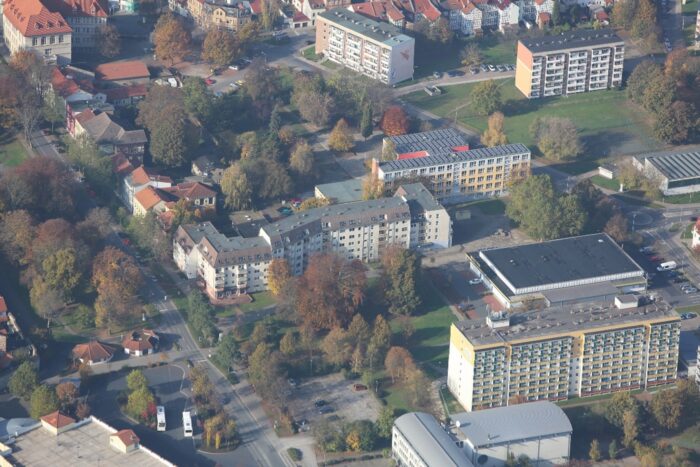 Aus der Luft sind mehrere Wohnblöcke, Einfamilienhäuser und Straßen zwischen herbstlich gefärbten Bäumen in einem ruhigen Stadtviertel am Rand der Innenstadt zu sehen.